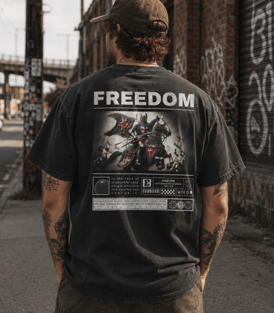 A man viewed from behind wearing a faded black graphic t-shirt with a large 'FREEDOM' print and motorcycle illustration on the back, standing on a city street.