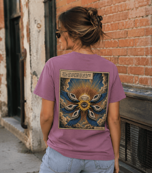 A woman viewed from behind wearing a mauve-purple graphic t-shirt with a large detailed spiritual design on the back, standing outdoors against a brick wall.