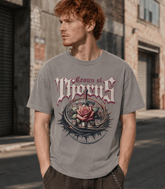 A man wearing a gray graphic t-shirt with a 'Crown of Thorns' design, standing in an outdoor urban setting with brick buildings.