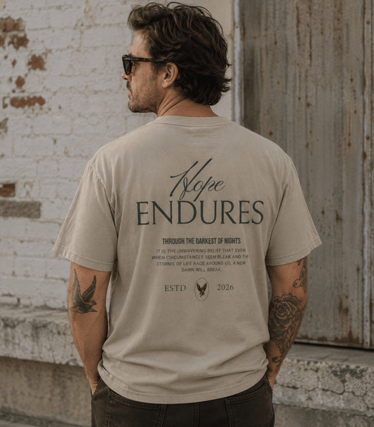 A man wearing a beige t-shirt with a dark gray graphic print on the back, photographed from behind against a rustic white brick wall and weathered metal door.