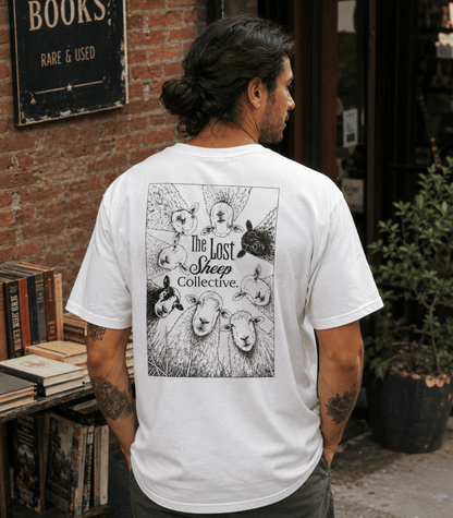 A man viewed from behind wearing a white graphic t-shirt with a black illustration of sheep and the text 'The Lost Sheep Collective' on the back, standing in front of a brick wall and bookshelf.