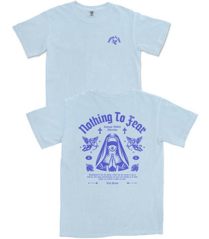A light blue short-sleeve t-shirt shown from both the front and back. The front features a small blue graphic on the left chest, and the back features a large blue graphic with the text 'Nothing To Fear', a hooded figure with an eye, wings, and additional small text.
