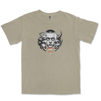 A beige crewneck t-shirt featuring a central graphic print of three stylized faces (a human face, a goat head, and a horned demon face) in gray, with small orange text below.