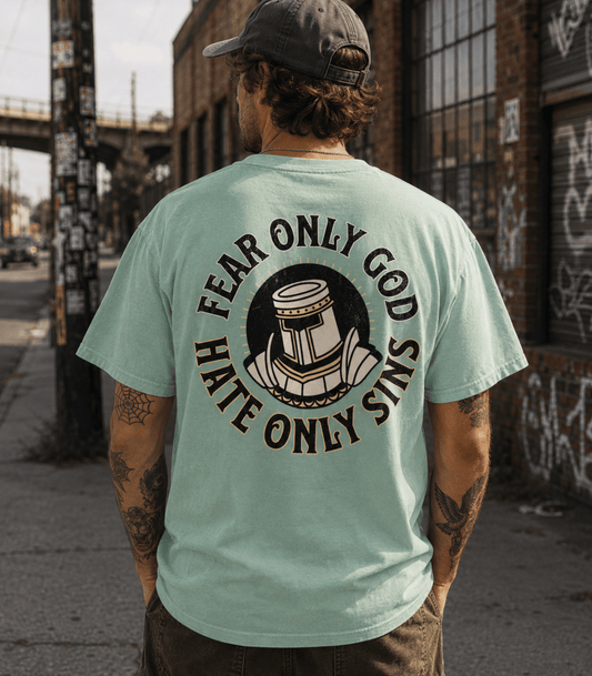 A man viewed from behind wearing a mint green t-shirt with a large black graphic print on the back. The graphic features a helmeted figure in the center with the text 'FEAR ONLY GOD HATE ONLY SINS' arched around it.