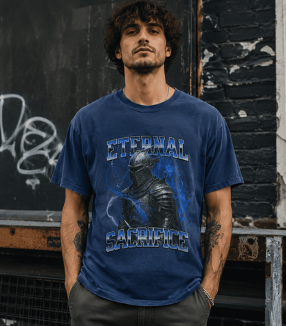 A man wearing a faded blue graphic t-shirt with 'ETERNAL SACRIFICE' and a knight design, standing in front of a dark brick wall.
